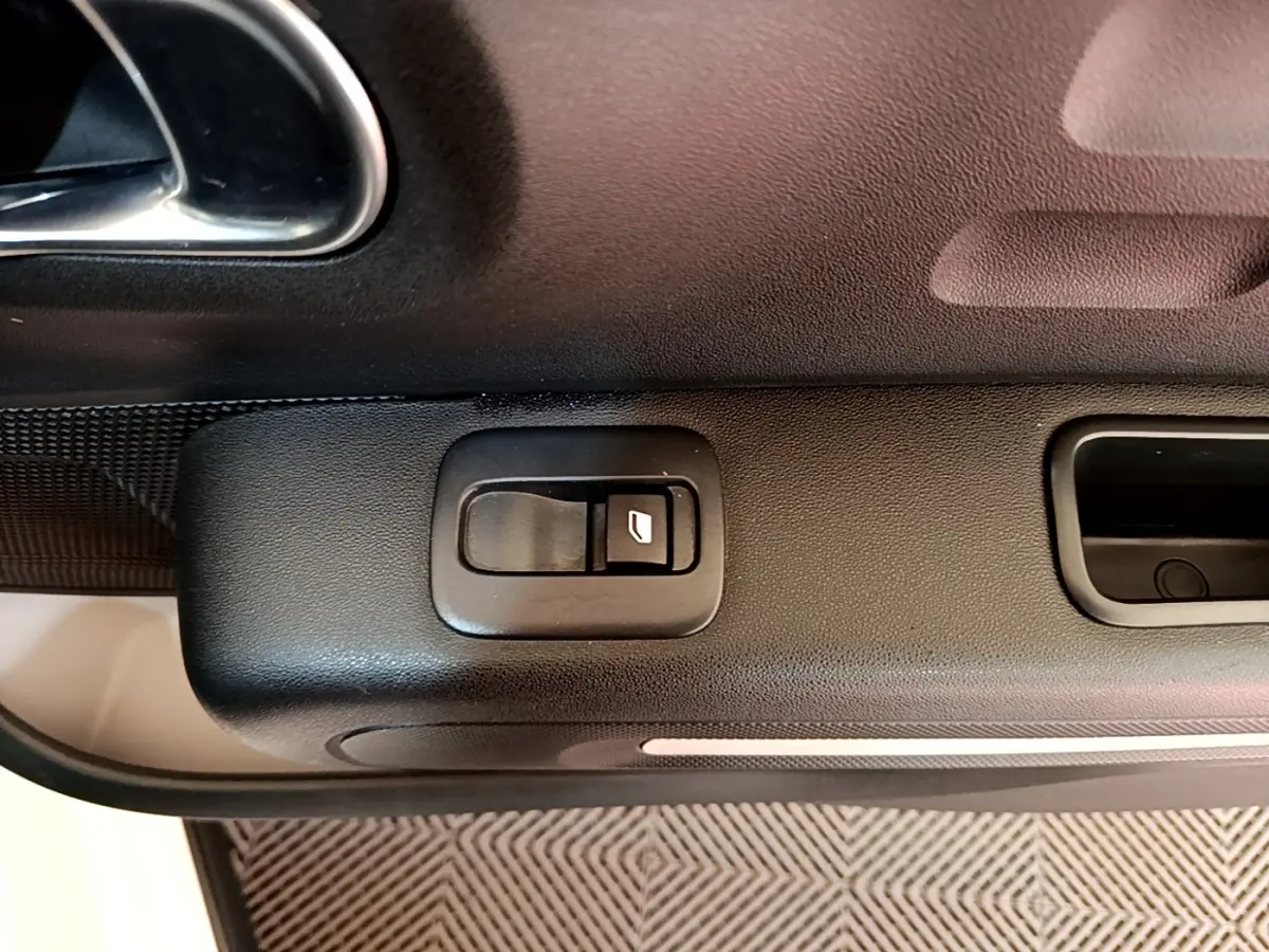 Gros plan sur la commande de lève-vitre noir sur la porte intérieure côté conducteur d'une Citroën C3 blanche.