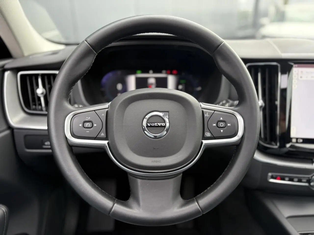 Volant noir 3 branches de Volvo XC60 T6 AWD PHEV 2024, vue frontale centrée sur les commandes intégrées.