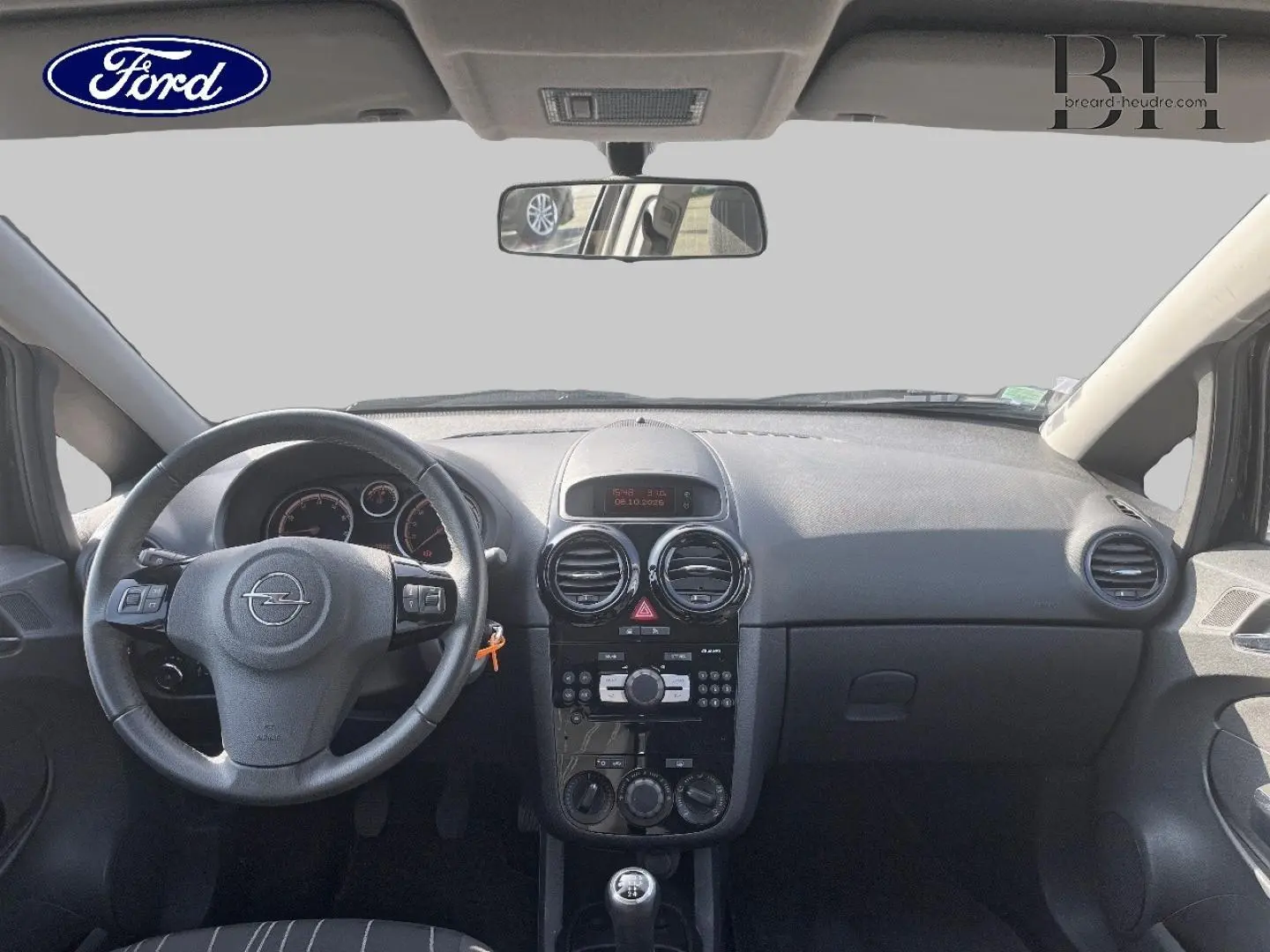 Vue intérieure avant de l’Opel Corsa noire de 2010, montrant le tableau de bord et le volant avec commandes intégrées.