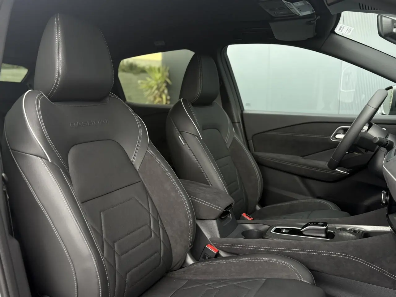 Intérieur du Nissan Qashqai 2025 côté conducteur et passager avec sièges Alcantara et cuir noirs, volant cuir et console centrale.