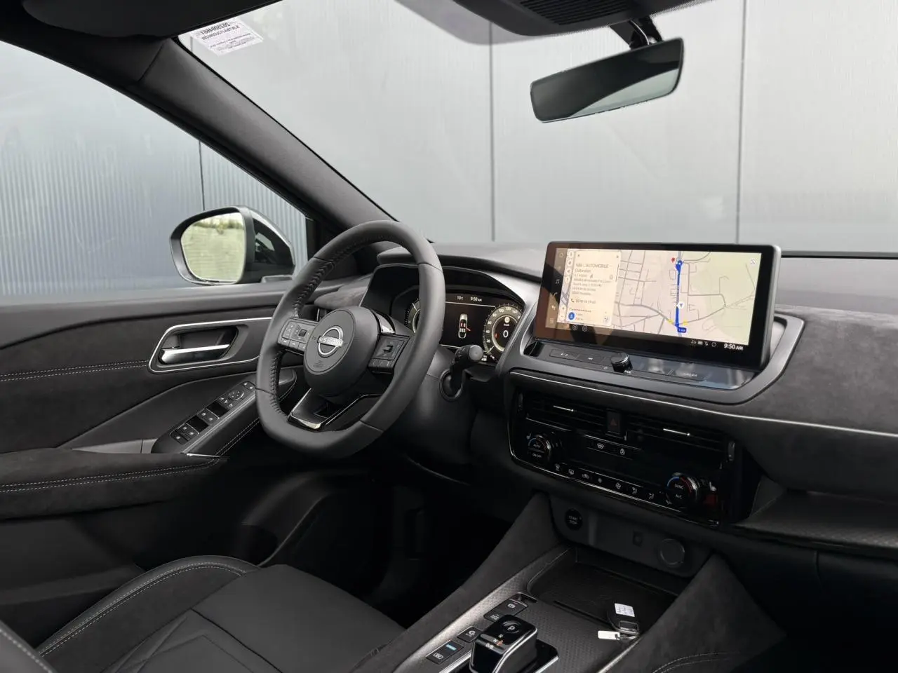 Vue intérieure côté conducteur du Nissan Qashqai 2025 gris Ceramic, avec volant cuir, écran tactile GPS et sellerie Alcantara.