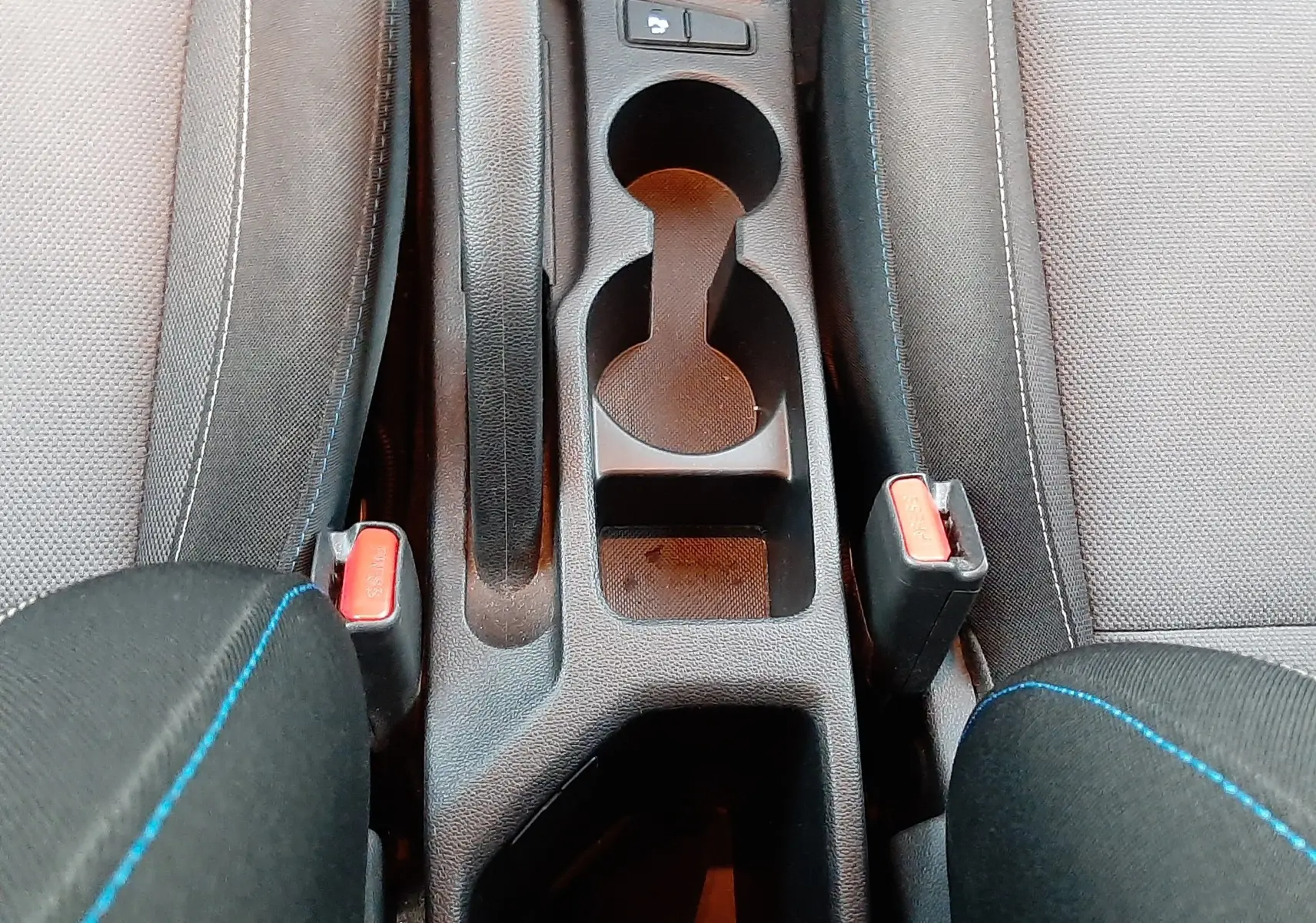 Vue plongeante sur la console centrale noire de la Hyundai i20 2016, avec porte-gobelets et frein à main entre sièges tissu gris.