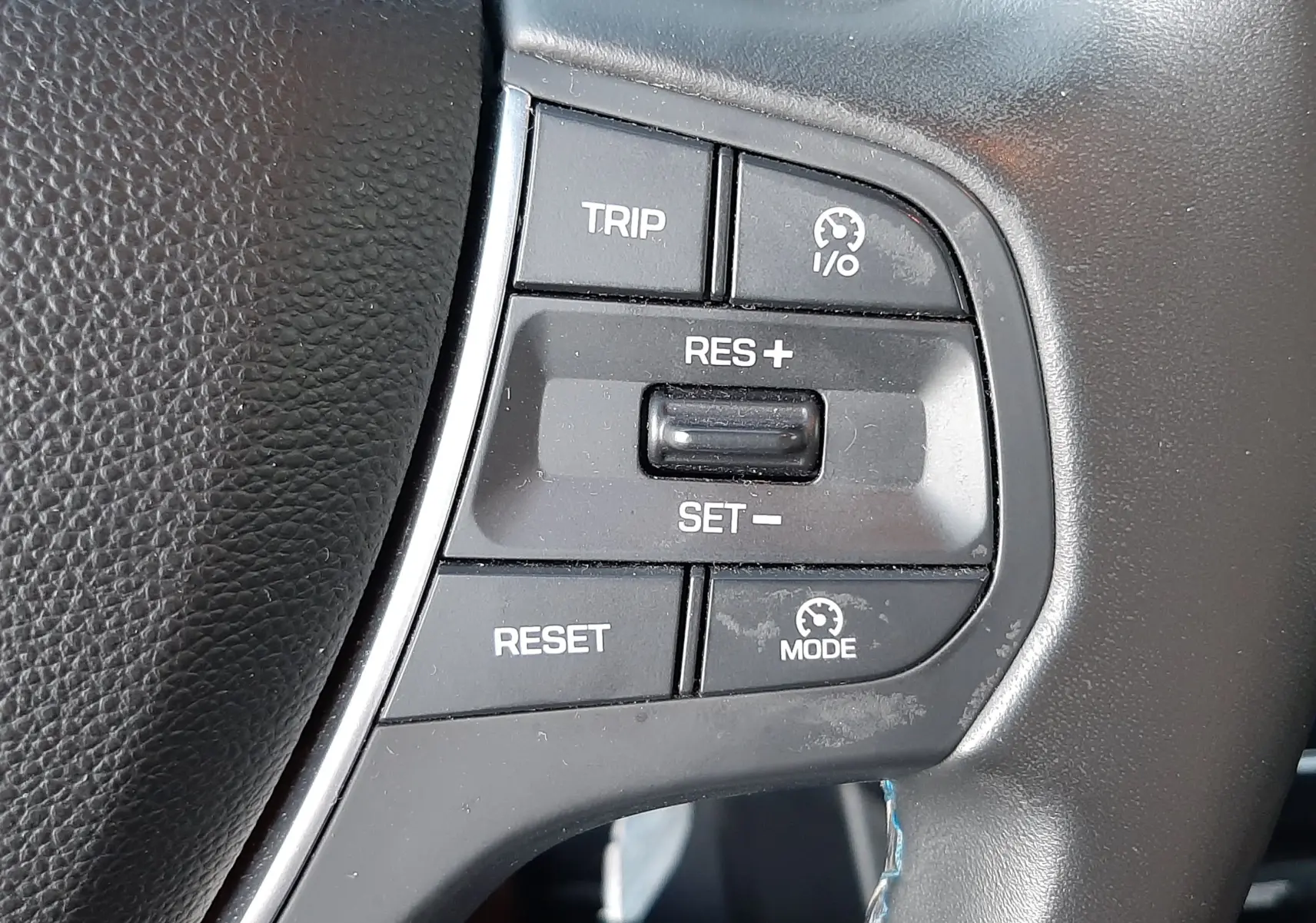 Gros plan sur les commandes de régulateur de vitesse du volant en cuir noir de la Hyundai i20 blanche, version 2016.