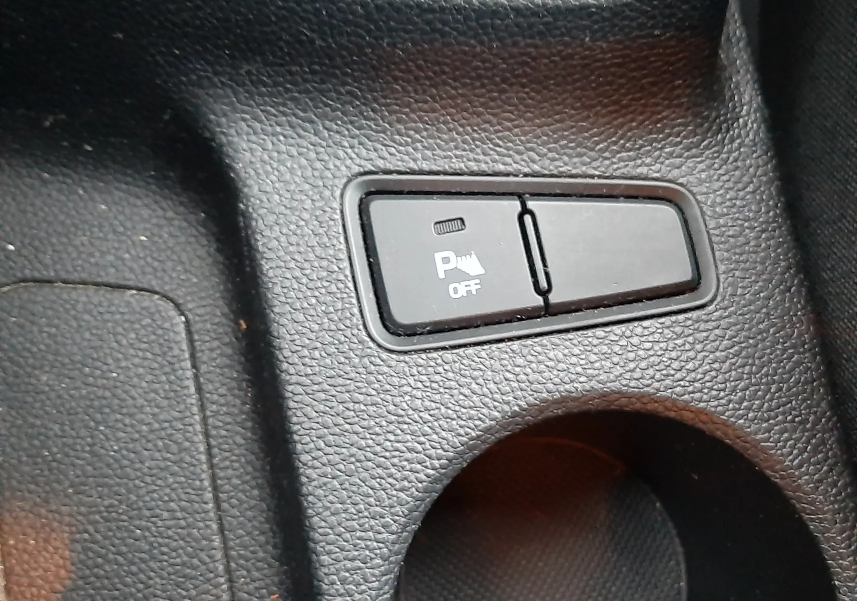 Gros plan sur le bouton de désactivation de l'aide au stationnement dans l'habitacle noir d'une Hyundai i20 blanche.
