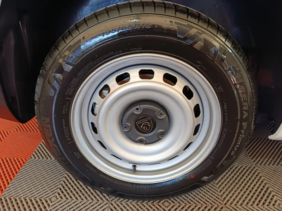 Gros plan sur la roue acier grise avec logo Peugeot au centre du Peugeot Partner blanc, vue côté droit.