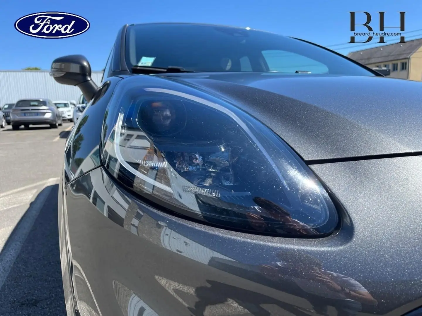 Gros plan sur le phare avant gauche du Ford Puma 2024 gris Solar métallisé sous un ciel dégagé.