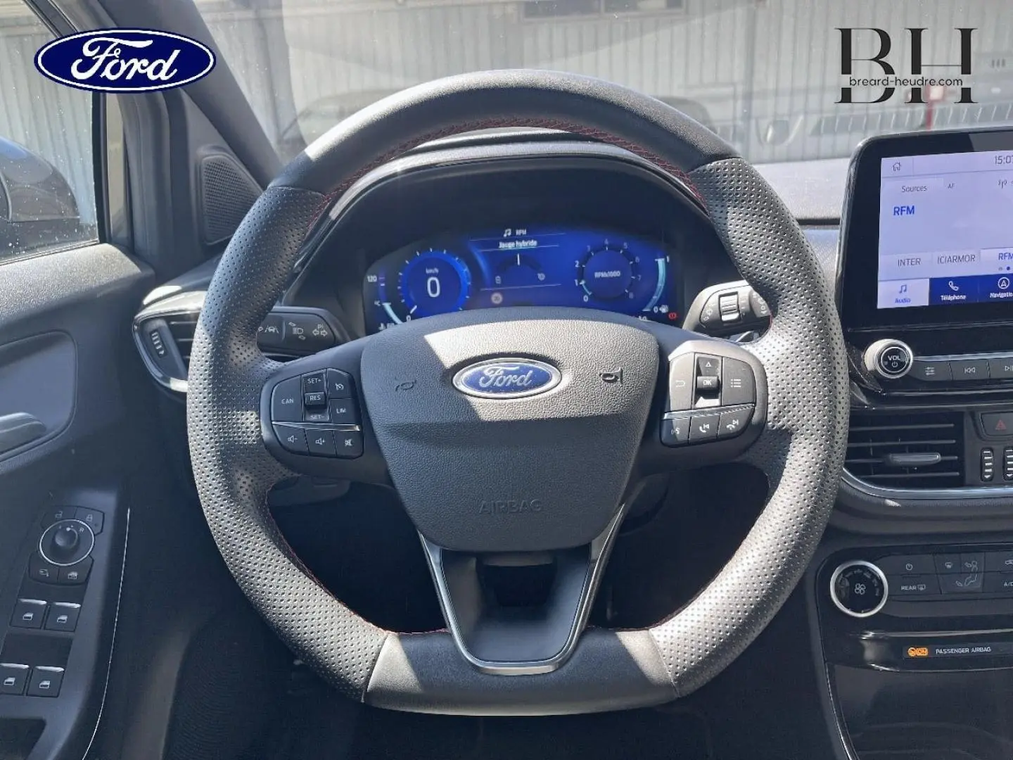 Vue intérieure centrée sur le volant perforé avec surpiqûres rouges du Ford Puma 2024, tableau de bord digital et écran tactile.