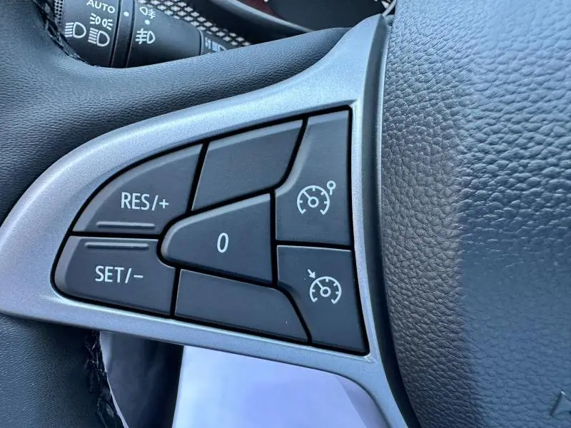 Gros plan sur les commandes de régulateur de vitesse au volant noir de la Dacia Sandero beige Safari 2025.