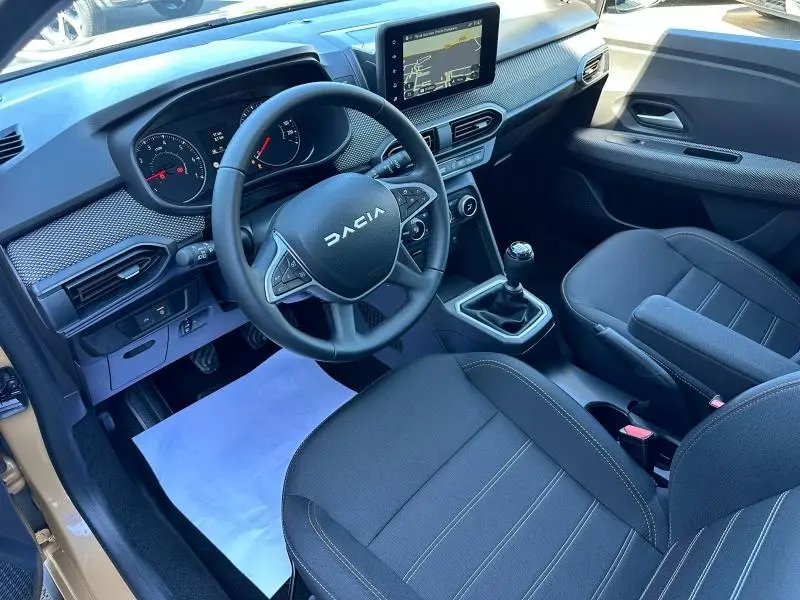 Vue intérieure avant droite du Dacia Sandero beige Safari, volant multifonction et écran tactile central visibles.