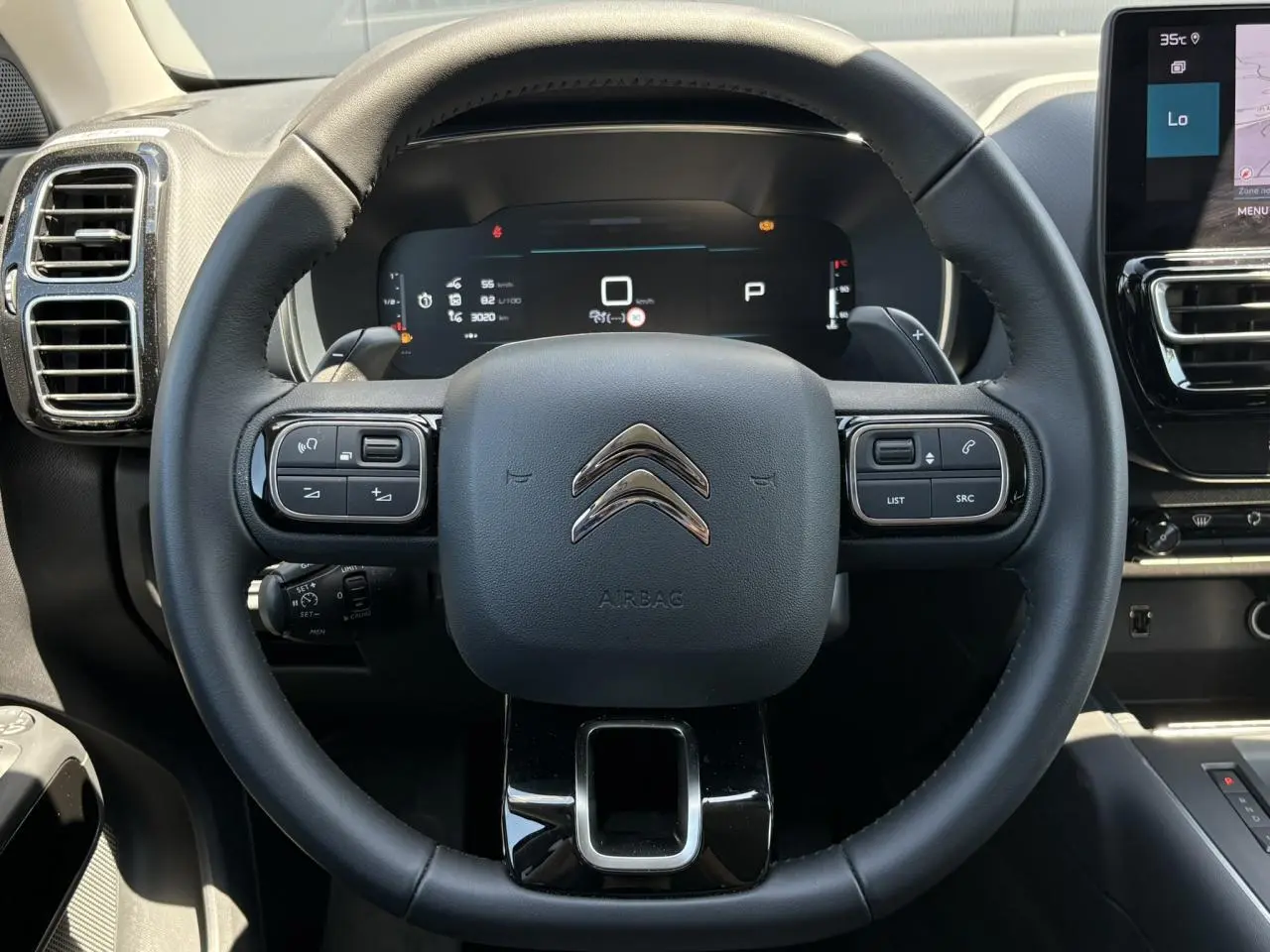 Vue centrée sur le volant noir du Citroën C5 Aircross Hybrid 2025 avec commandes intégrées et tableau de bord numérique.