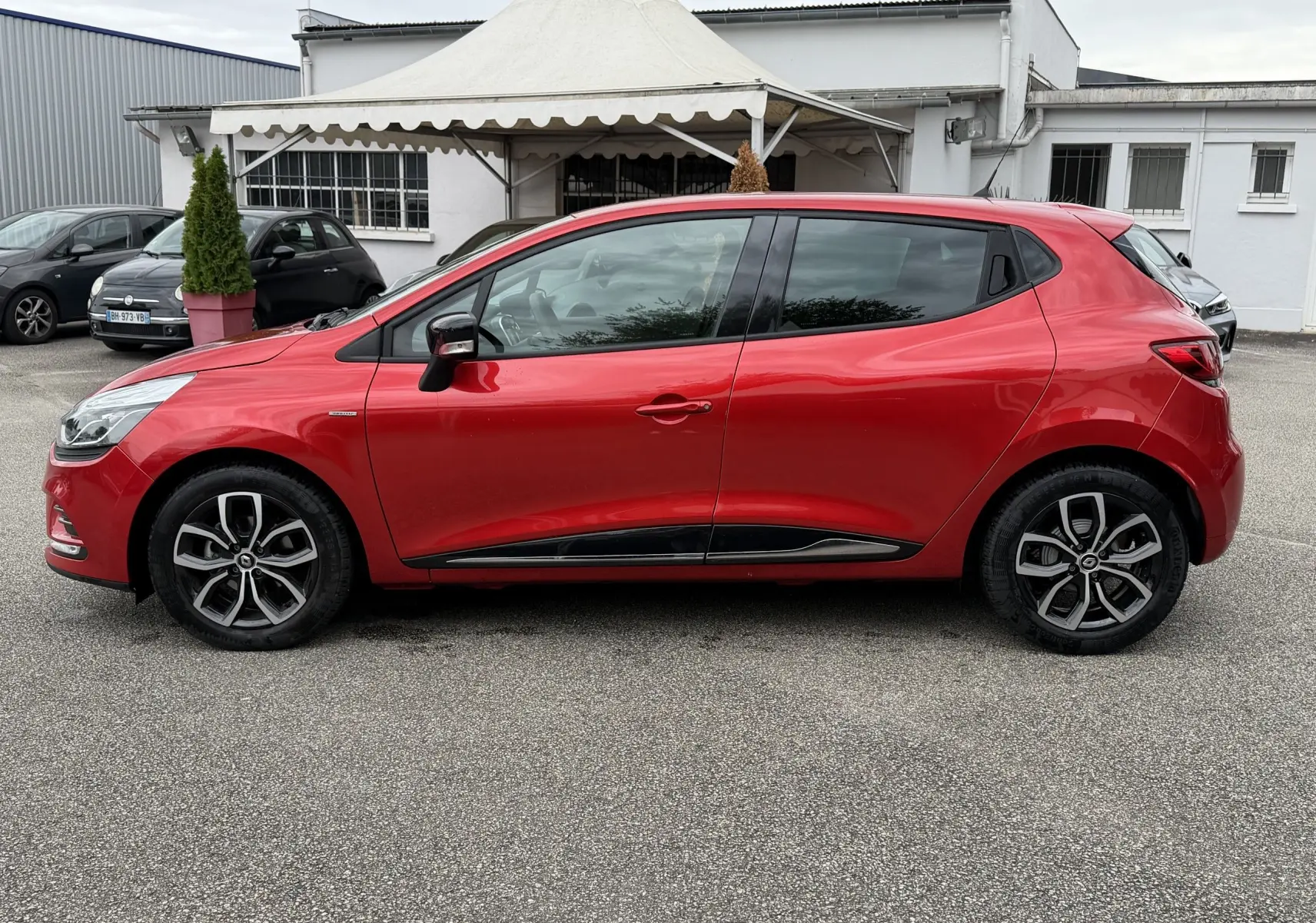 Profil côté gauche d'une Renault Clio IV Limited TCE 90 rouge flamme de 2017 avec jantes alliage et vitres teintées.