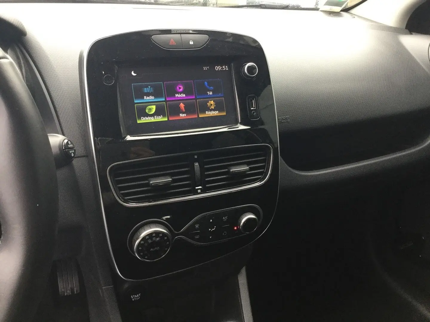 Vue intérieure centrée sur la console centrale noire brillante avec écran tactile et commandes de climatisation d'une Renault Clio IV Estate.