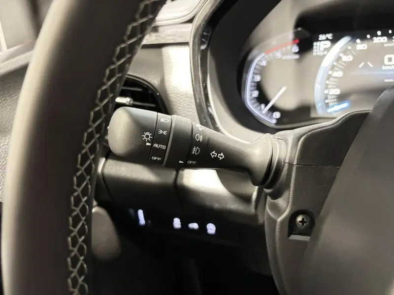 Gros plan sur le commodo d'éclairage à gauche du volant dans l'habitacle noir du pick-up Isuzu D-MAX 2025.