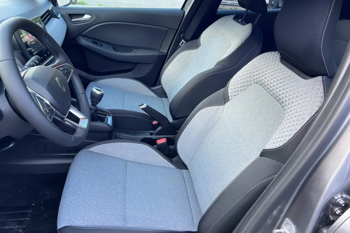Vue intérieure côté conducteur de la Renault Clio gris schiste 2025, sièges tissu bicolore et levier de vitesses manuel visible.