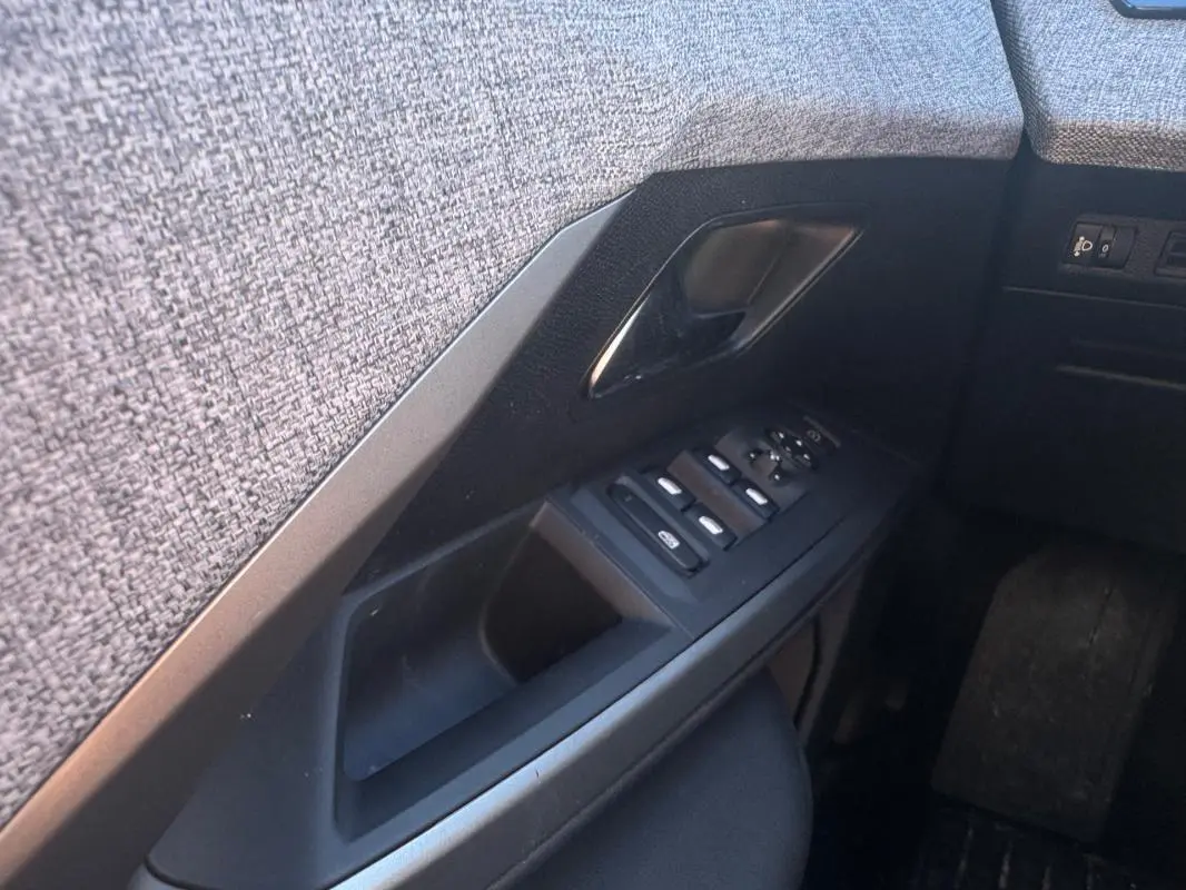 Gros plan sur la commande des vitres et la poignée intérieure côté conducteur du Peugeot 5008 gris Hybrid 145 e-DCS6 Allure 2025.