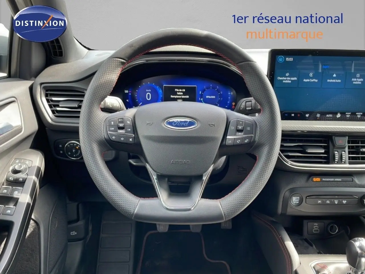 Vue intérieure avant centrée sur le volant cuir perforé avec coutures rouges, tableau de bord numérique et écran tactile Ford Focus SW gris lunaire.