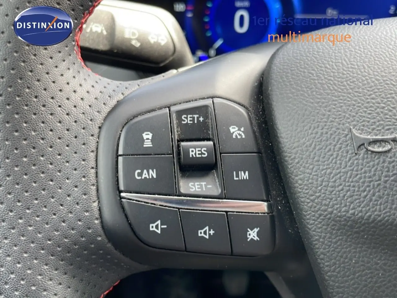 Gros plan sur les commandes noires du volant perforé avec surpiqûres rouges de la Ford Focus SW gris lunaire 2023.
