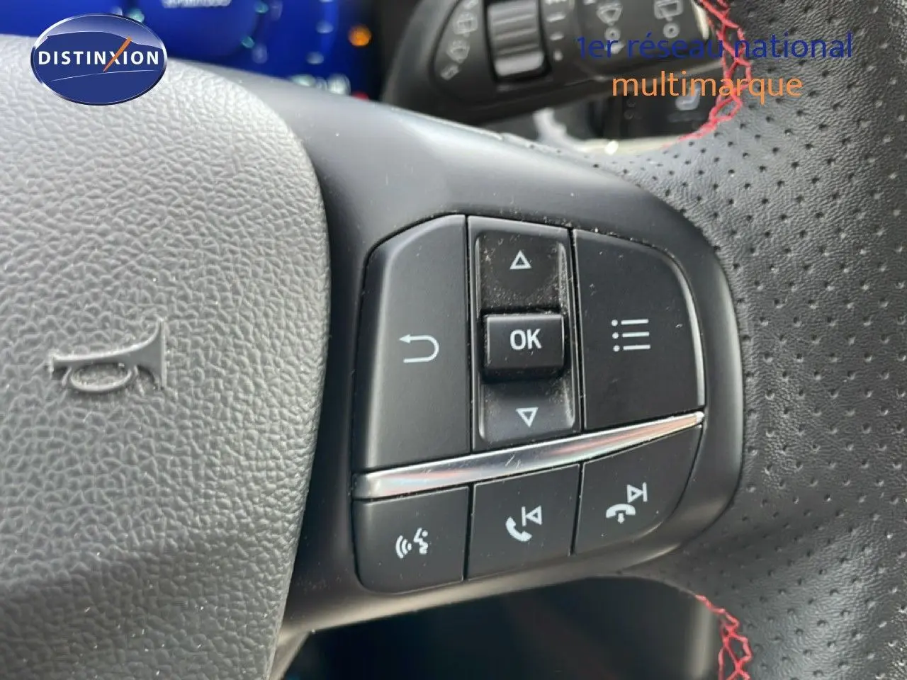 Gros plan sur les commandes multifonctions à droite du volant perforé avec surpiqûres rouges d'une Ford Focus SW gris lunaire 2023.