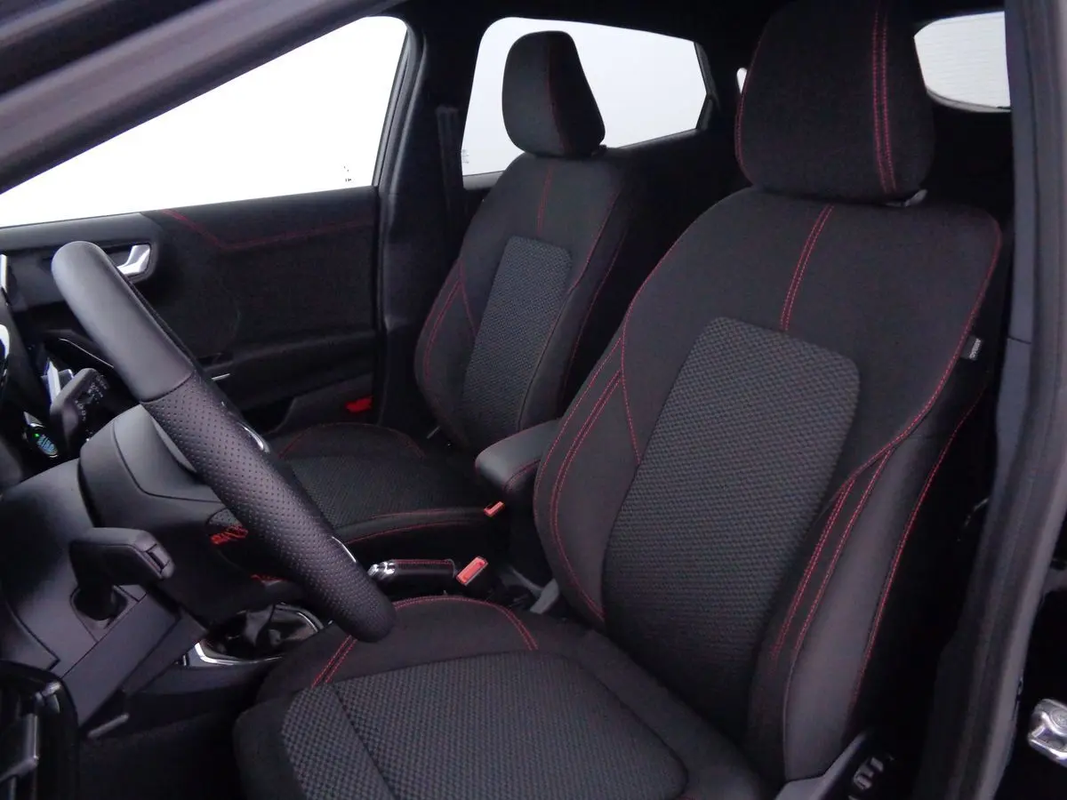 Vue intérieure côté gauche du Ford Puma 2022 noir agate, sièges tissu noir avec surpiqûres rouges et volant cuir perforé.