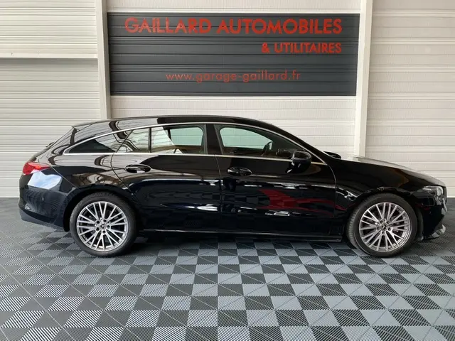 Profil latéral droit d'une Mercedes Classe CLA Shooting Brake noire, élégante et moderne, sur sol damier intérieur showroom.