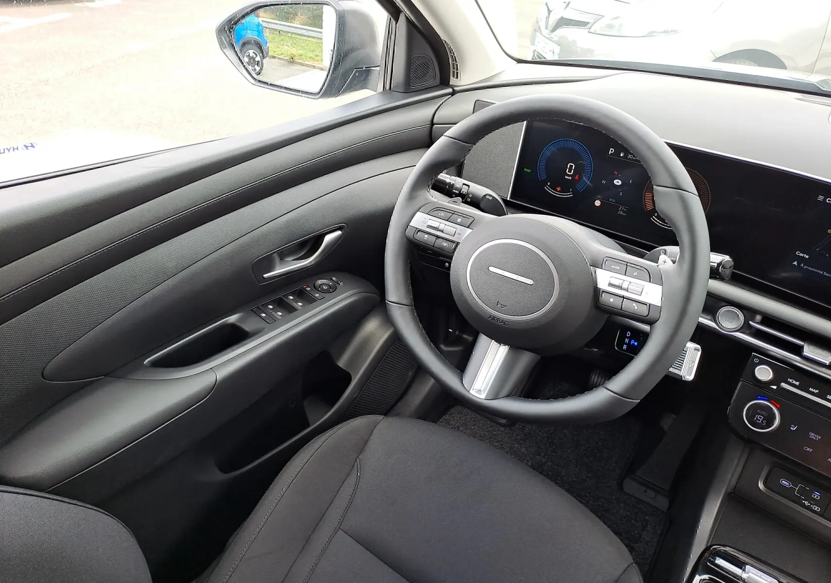 Intérieur côté conducteur du Hyundai Tucson 2025 gris, volant multifonction et tableau de bord numérique moderne.