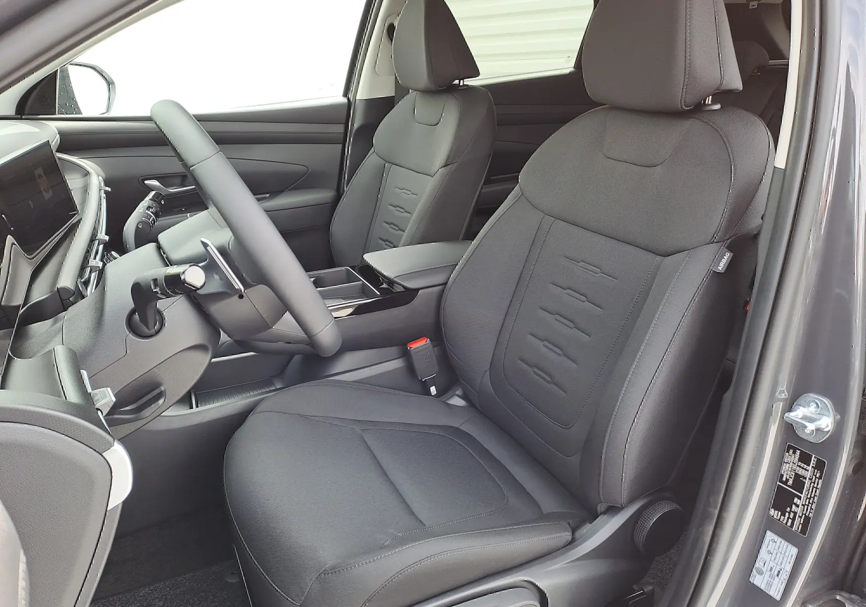 Intérieur côté conducteur du Hyundai Tucson 2025 gris Ecotronic, sièges tissu noir avec détails cousus et tableau de bord moderne.