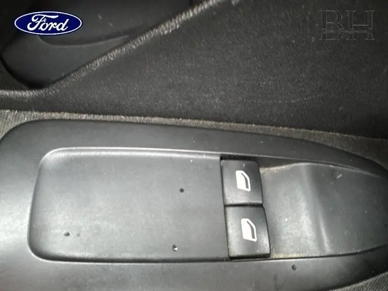 Gros plan sur les commandes de lève-vitres avant gauche d'une Peugeot 208 blanc banquise, intérieur tissu noir.