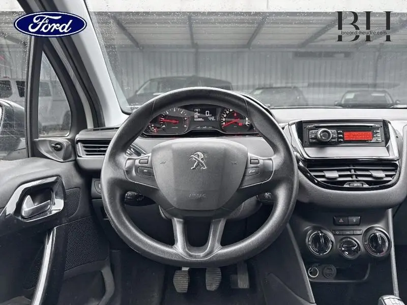Vue intérieure du tableau de bord et volant Peugeot 208 blanc Banquise, avec commandes au volant et console centrale noire.