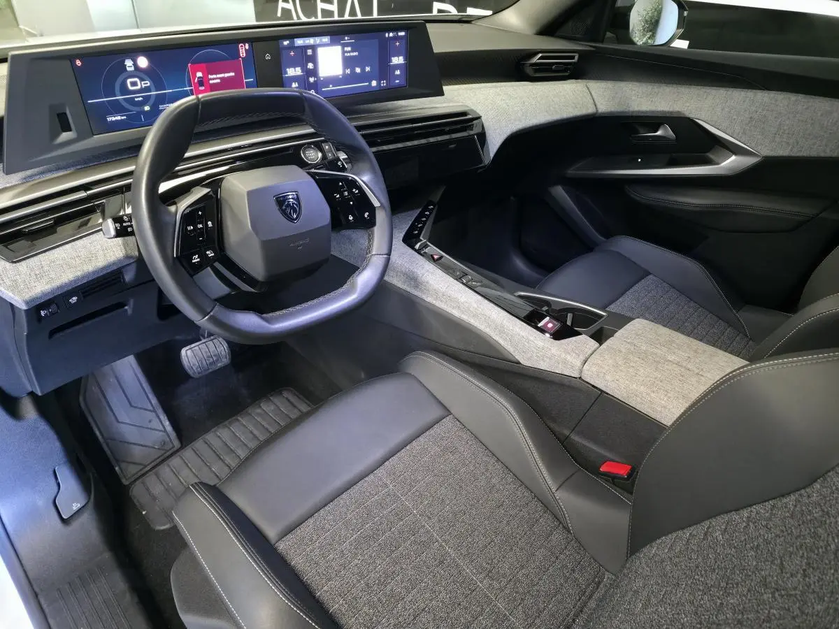 Intérieur avant droit du Peugeot 3008 blanc 2025, volant compact cuir noir, tableau de bord numérique et sellerie tissu gris.