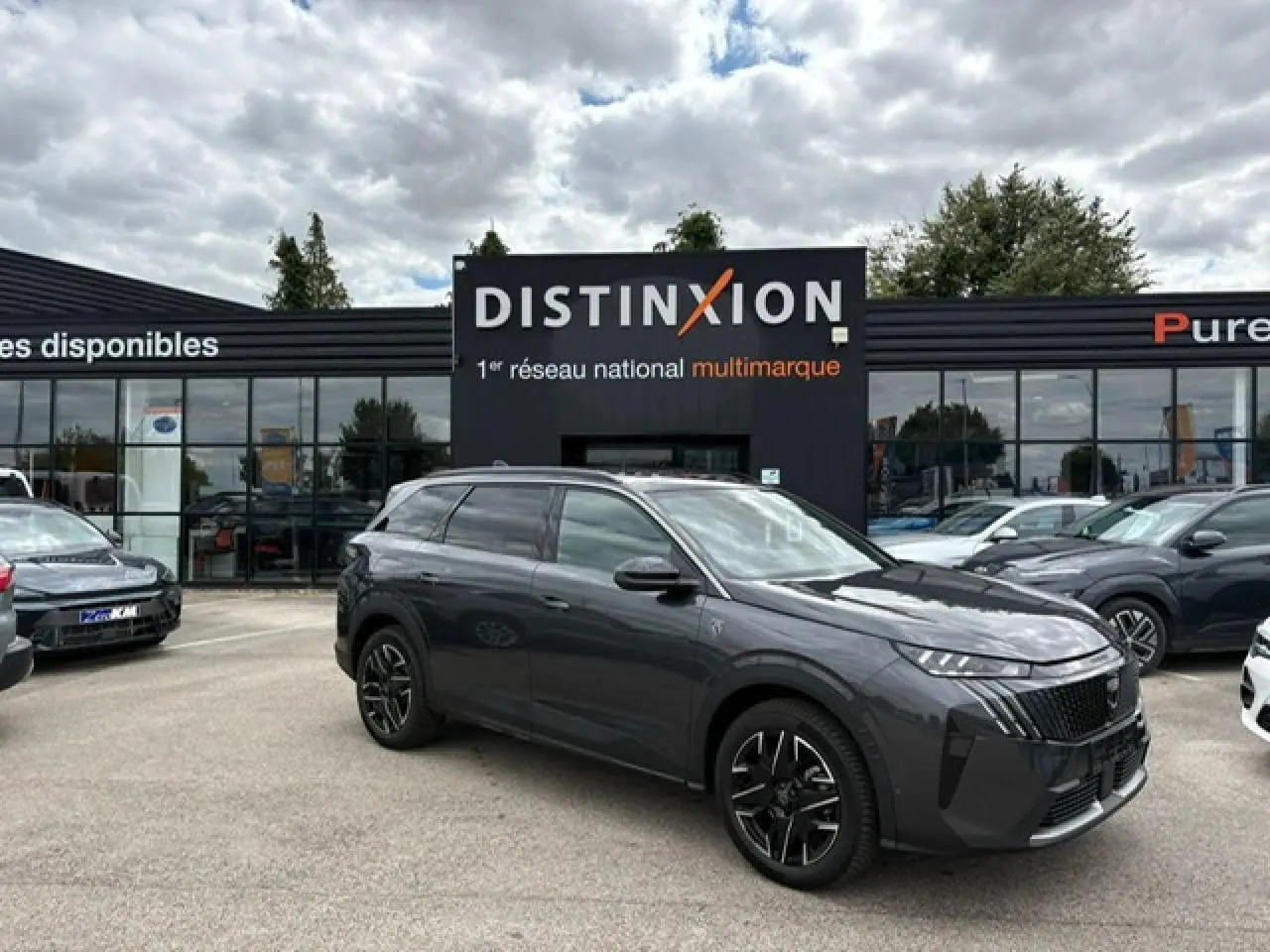 Peugeot 5008 gris titane avec toit noir, vue 3/4 avant droit sur parking devant concession Distinxion.