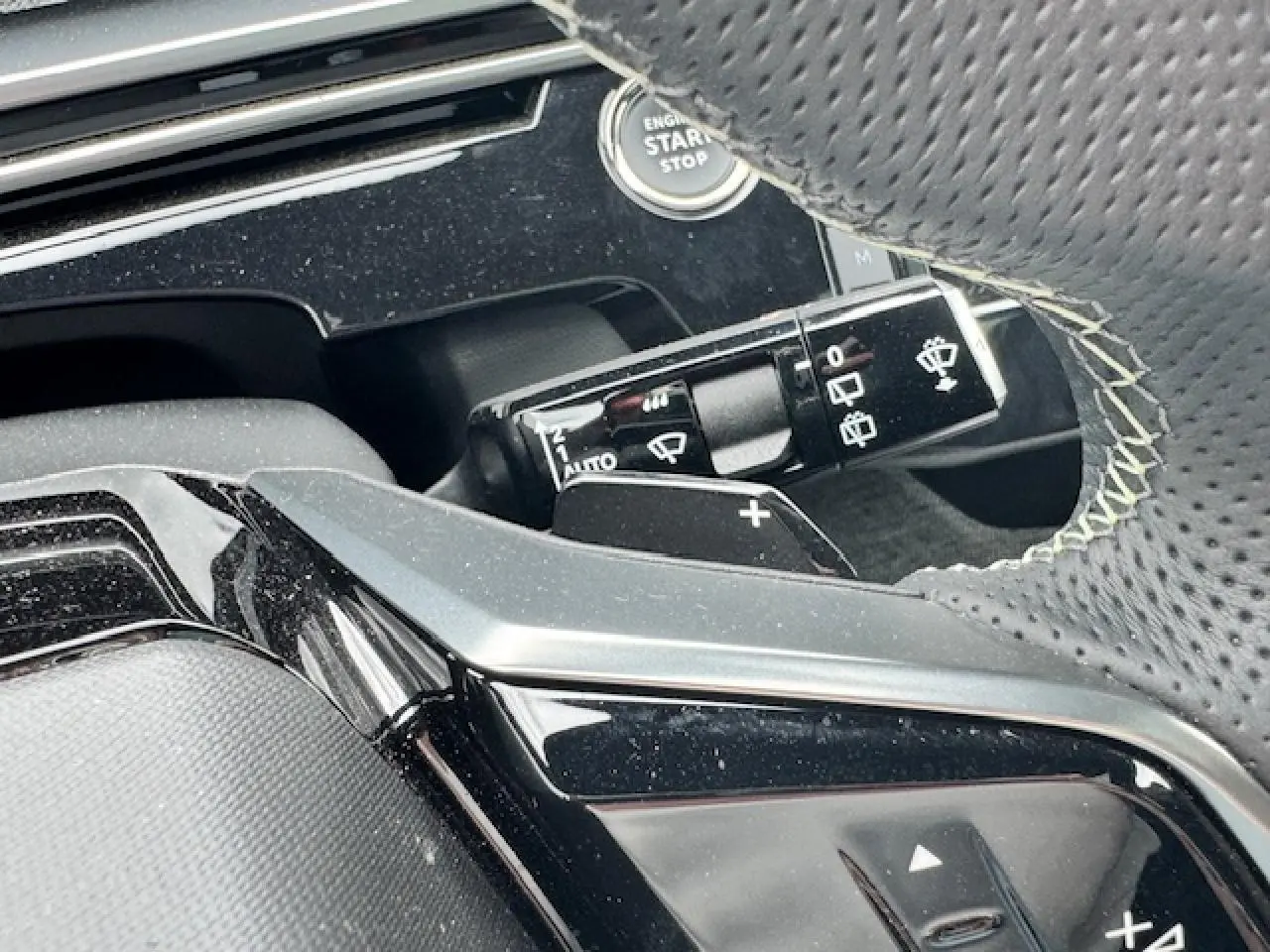 Détail du volant perforé avec surpiqûres et commandes, bouton start/stop et manette d'essuie-glace du Peugeot 5008 gris titane.