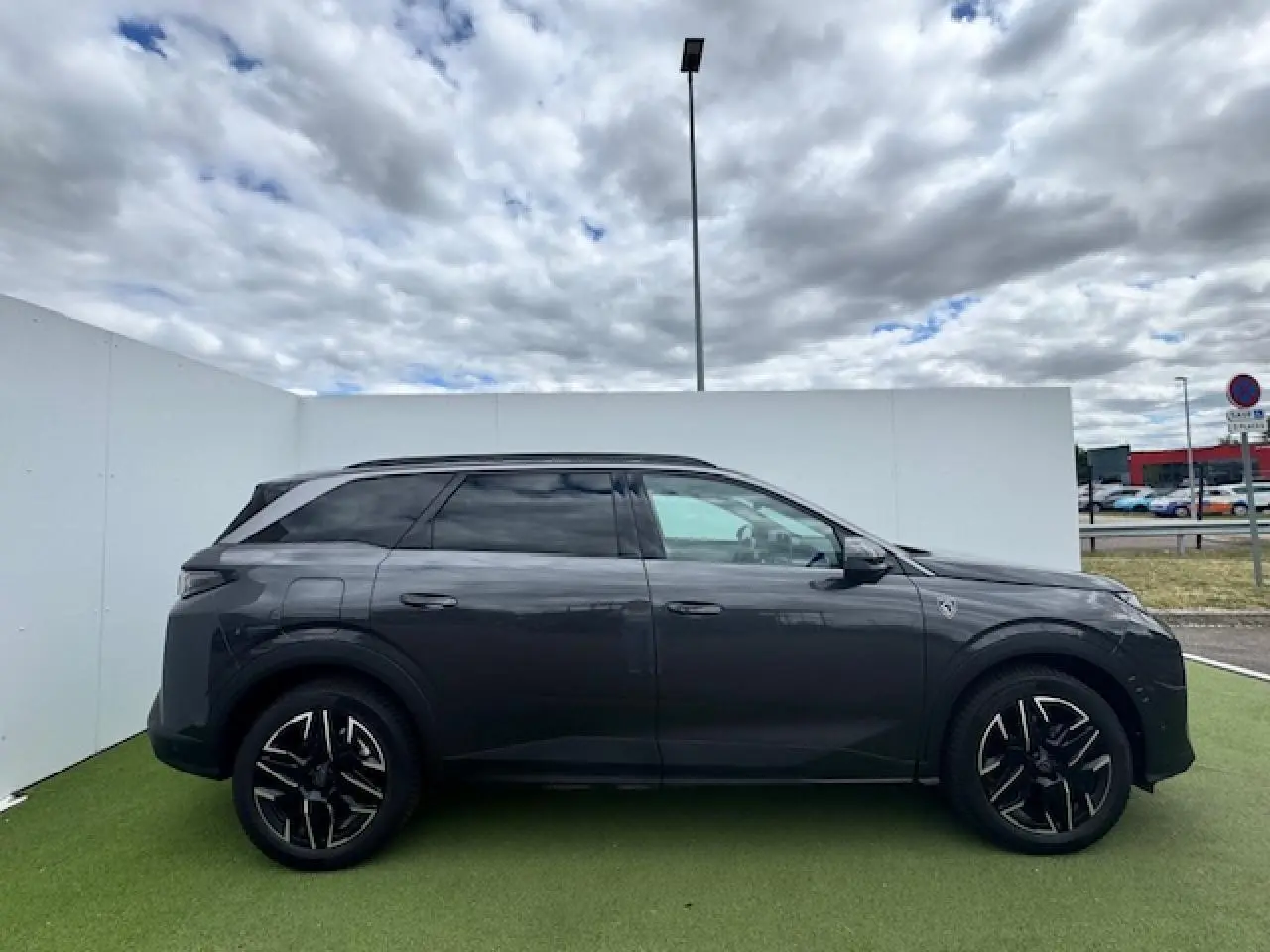 Profil côté droit du Peugeot 5008 gris titane avec toit noir et jantes alliage 19 pouces sur fond urbain.