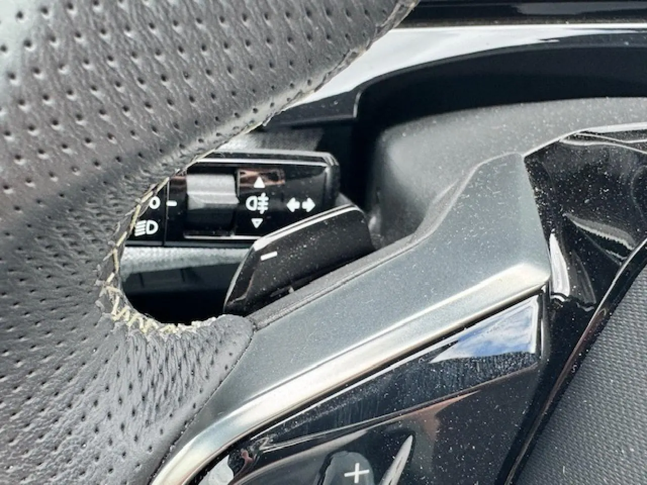 Détail du volant perforé gris avec commandes intégrées sur Peugeot 5008 gris titane 2024 hybride.