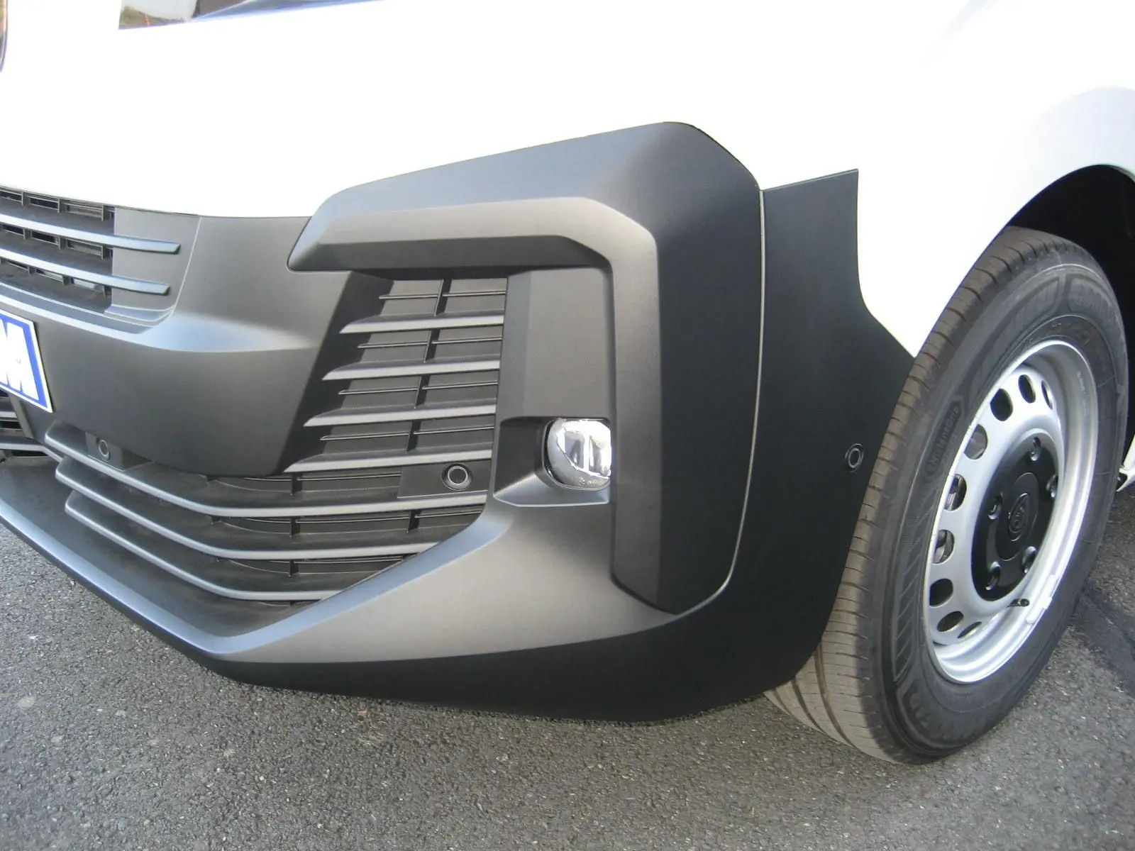 Gros plan sur le pare-chocs avant droit noir et la roue acier du Peugeot Expert Fourgon blanc.