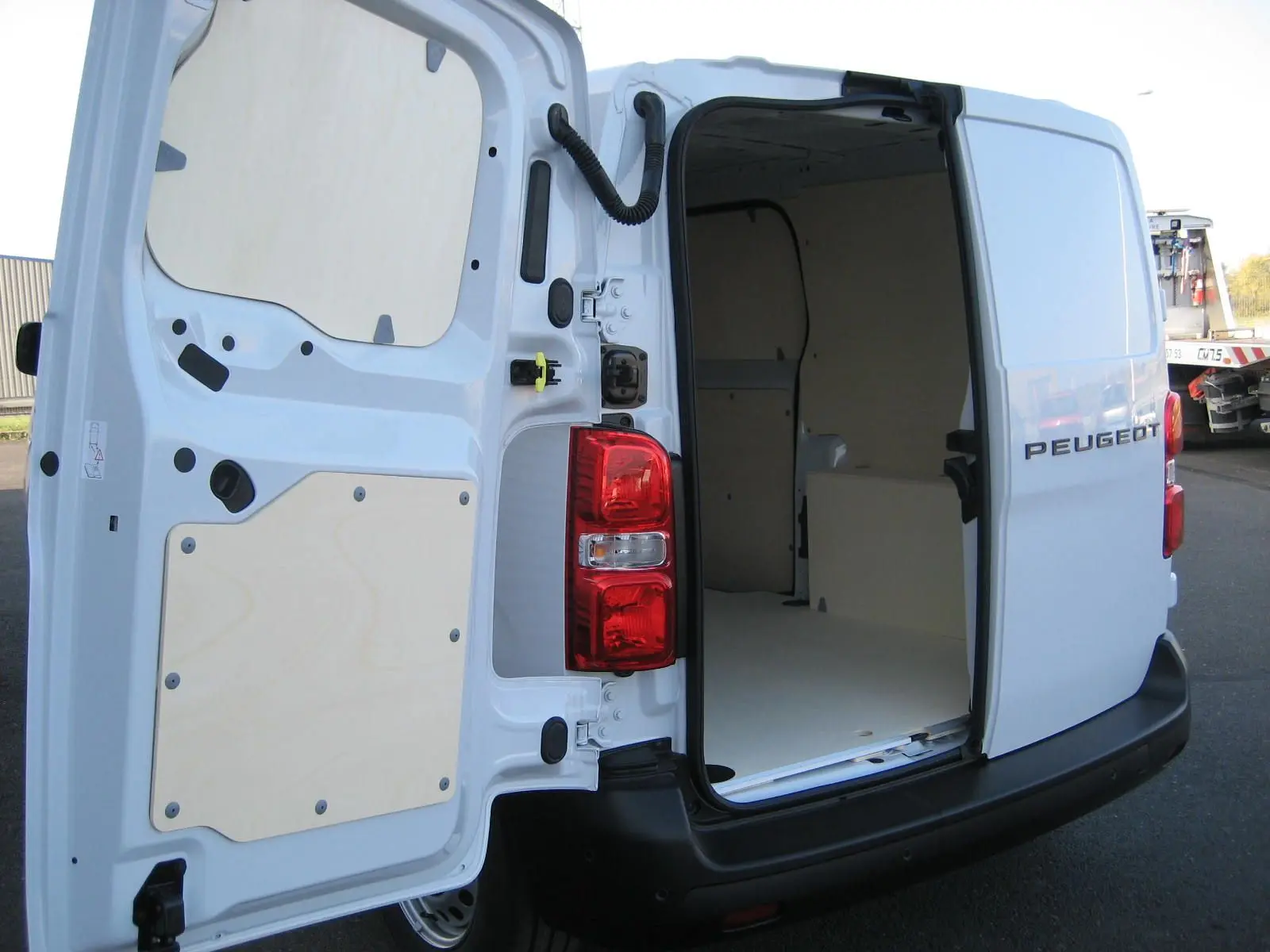 Vue arrière droite d'un Peugeot Expert Fourgon blanc 2025 avec portes ouvertes montrant l'intérieur vide et aménagement bois.