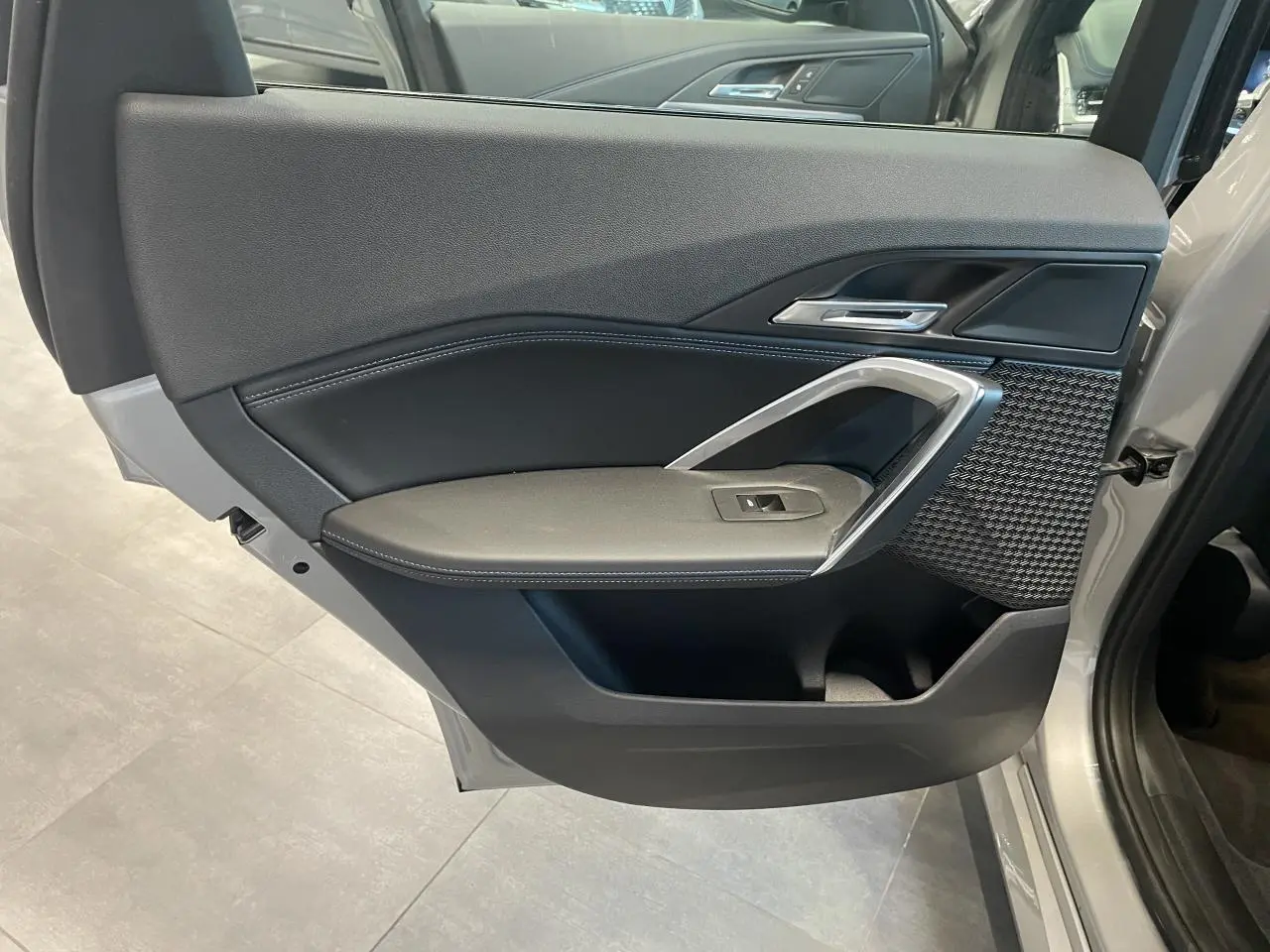 Vue rapprochée de la porte arrière gauche d’un BMW X1 xDrive 20d 2024 en Spacesilber Metallic avec garniture intérieure noire et inserts argentés.