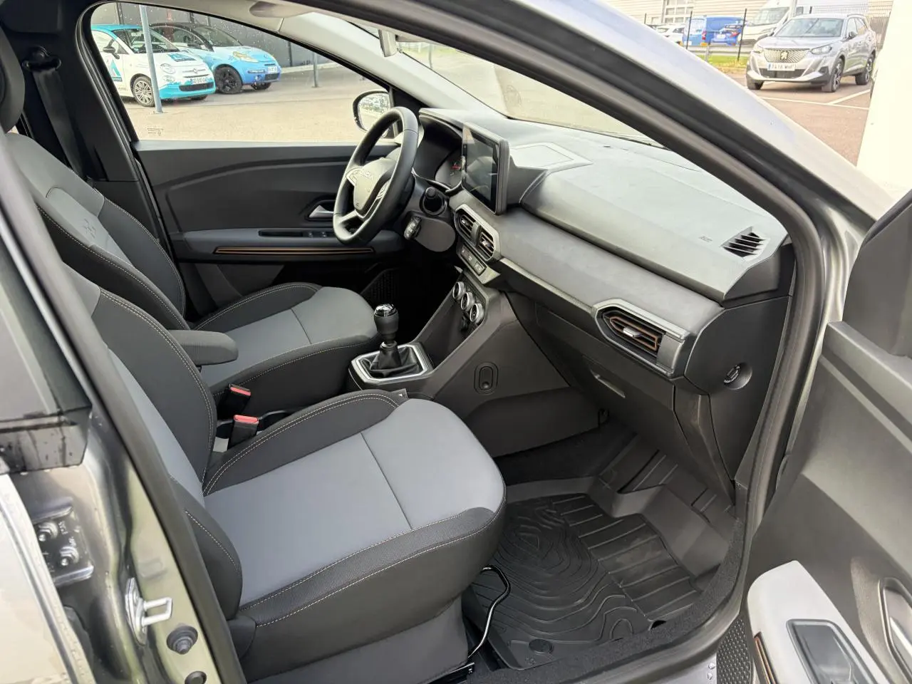 Vue intérieure côté conducteur de la Dacia Jogger gris schiste, montrant sièges et tableau de bord avec écran tactile.
