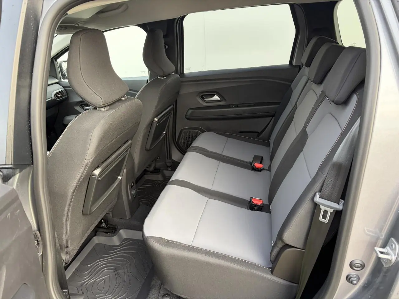 Vue intérieure côté droit sur la banquette arrière grise et noire du Dacia Jogger 2025 avec tablettes aviation au dos des sièges avant.
