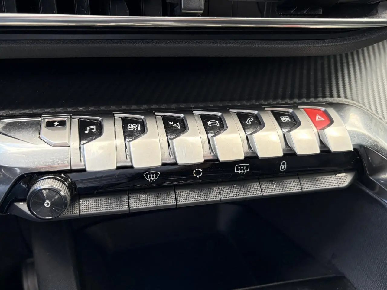 Gros plan sur la rangée de boutons métalliques du tableau de bord noir du Peugeot 3008 Plug-in Hybrid 2024.
