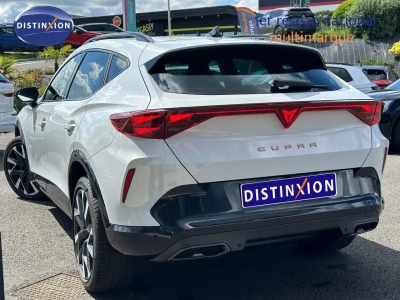 Vue 3/4 arrière droite d'un CUPRA Formentor blanc Nevada métallisé avec feux arrière LED reliés et jantes alu noires.