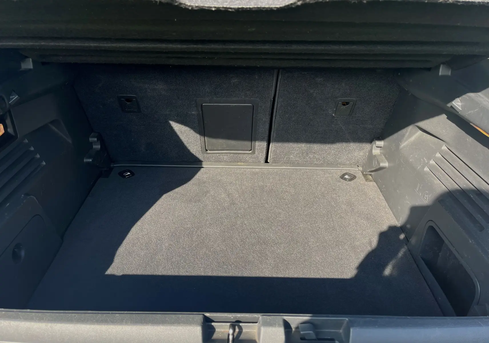 Coffre spacieux et propre du Peugeot 3008 gris clair, vue intérieure arrière avec tapis et habillage noir.