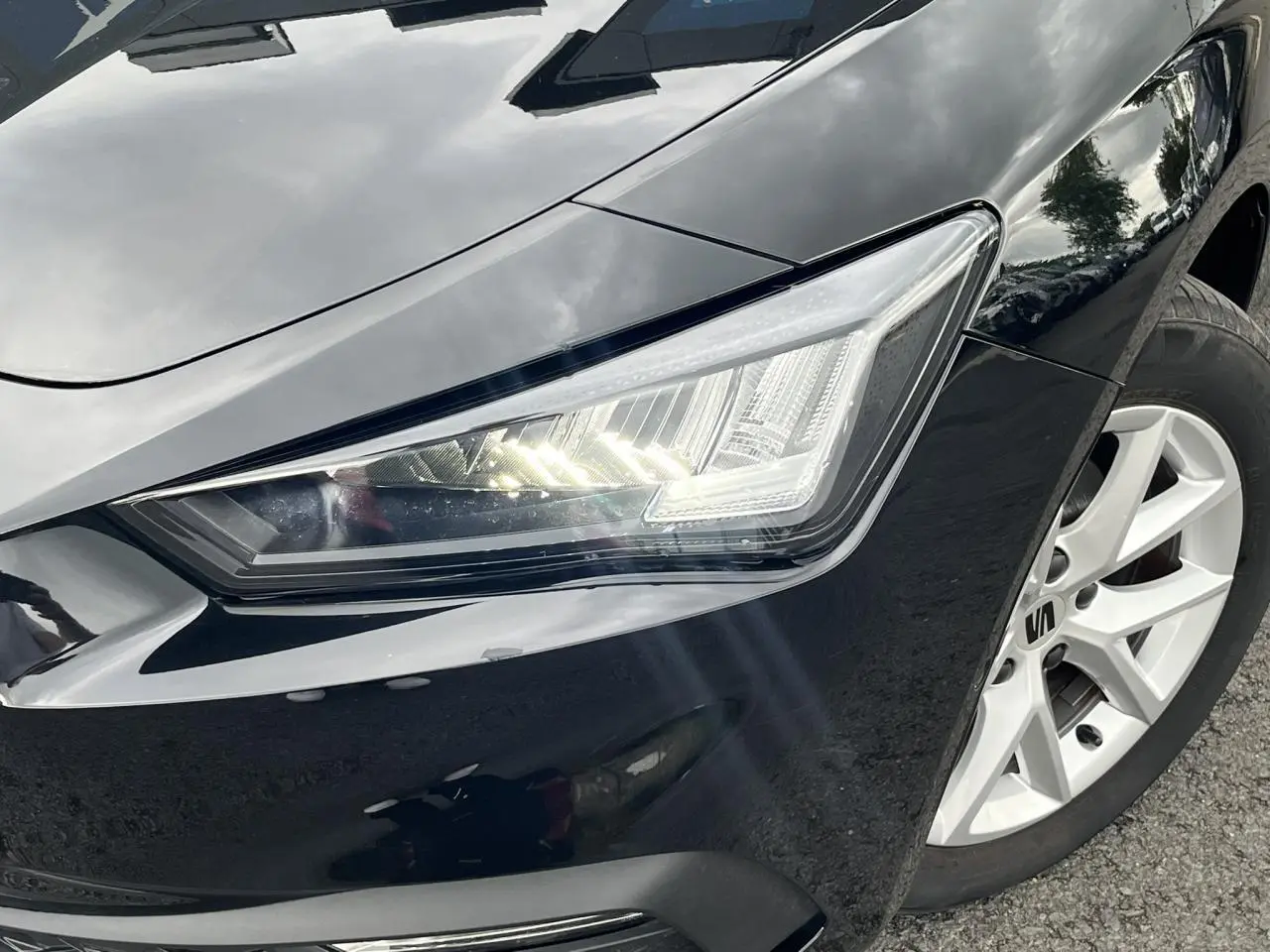 Gros plan sur le phare avant droit et la jante alliage blanche d'une SEAT LEON noire Minuit 2024.