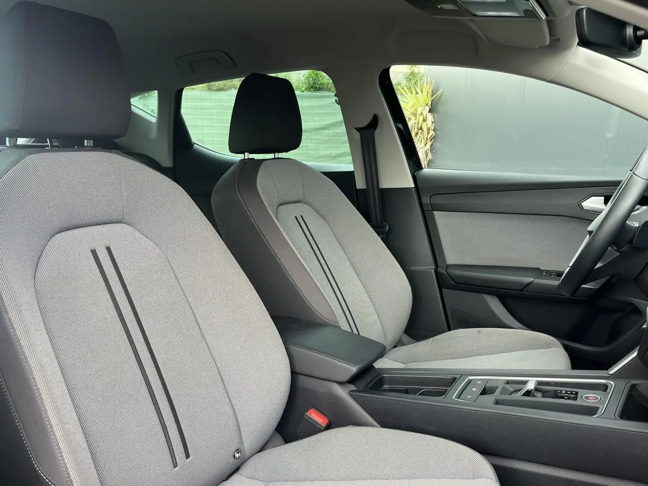 Intérieur de la SEAT LEON 2024 vu côté droit, sièges tissu gris clair avec accoudoir central noir.