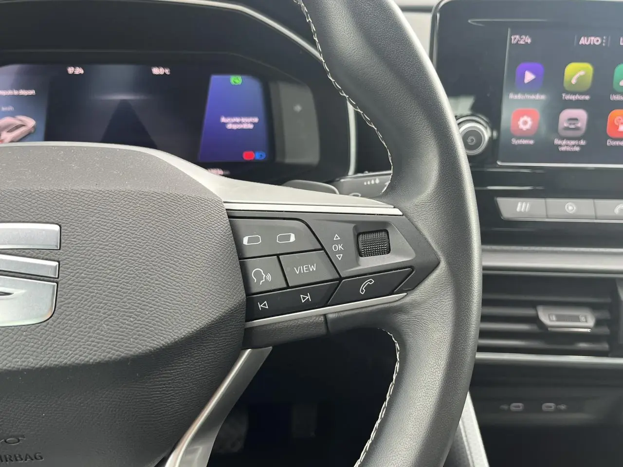 Gros plan sur le volant cuir multifonction de la SEAT LEON 2024, avec commandes intégrées et écran digital en arrière-plan.