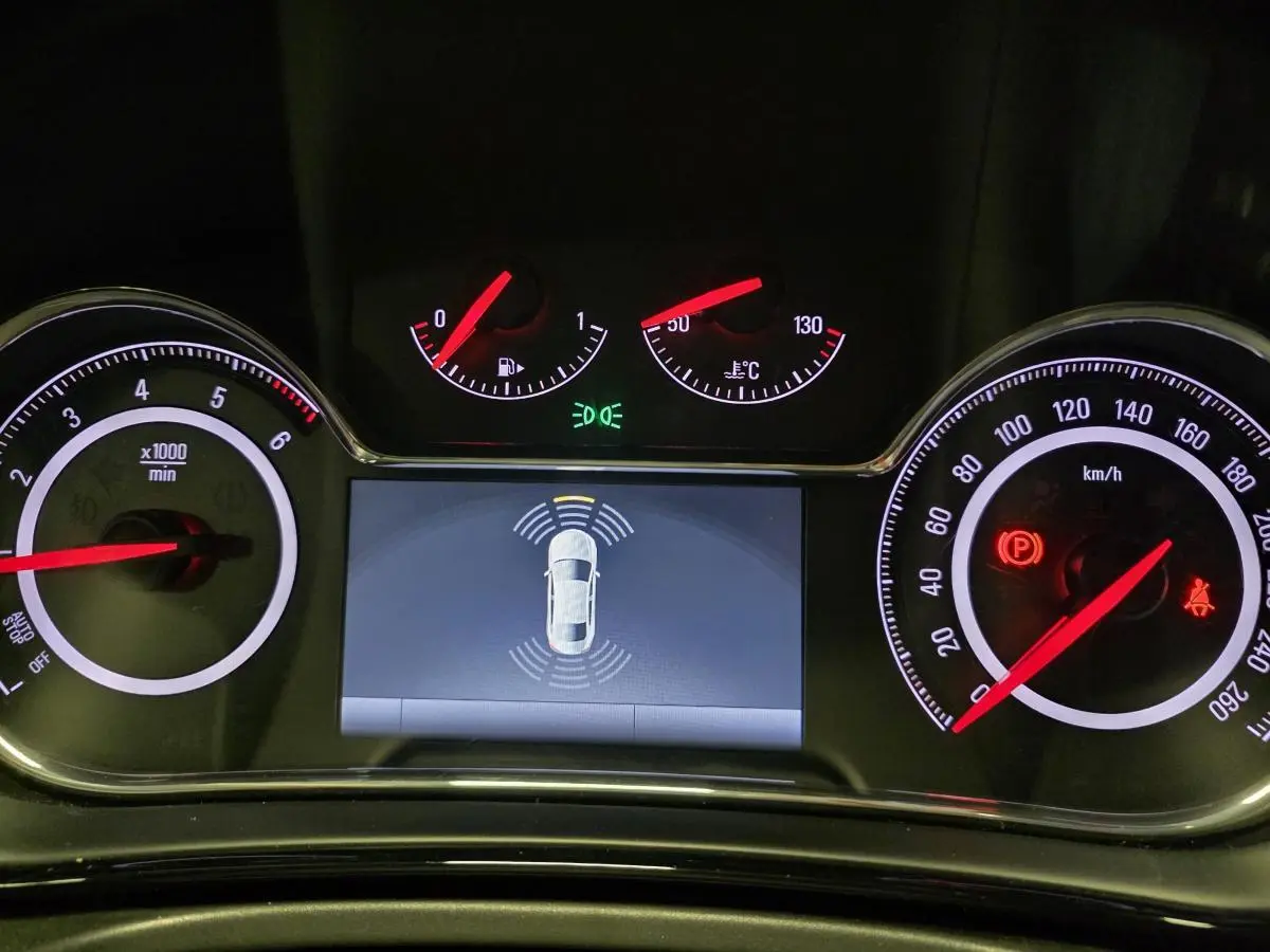 Tableau de bord noir de l'Opel Insignia 2016 avec affichage d'aide au stationnement et compteurs éclairés rouges.