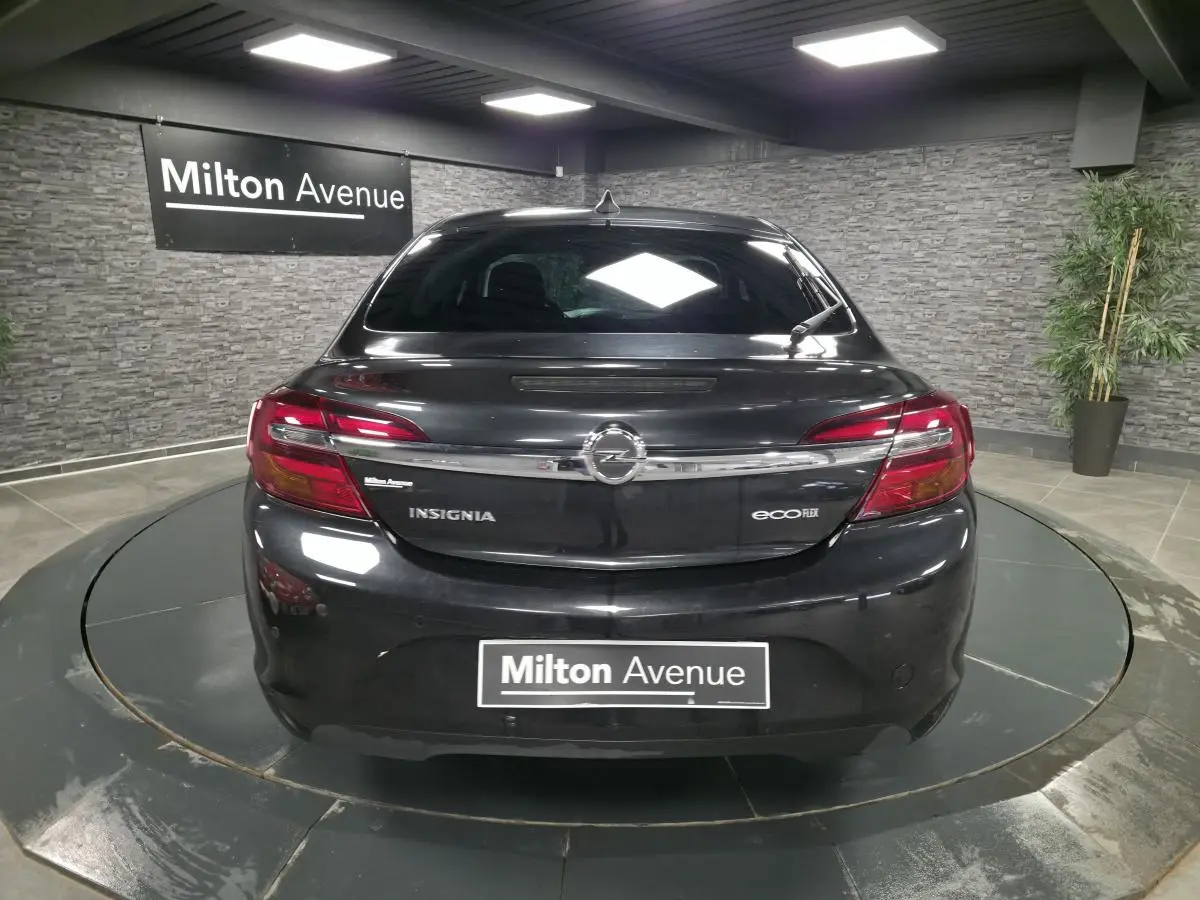 Vue arrière d'une Opel Insignia noire avec feux rouges et logo chromé dans un showroom intérieur.