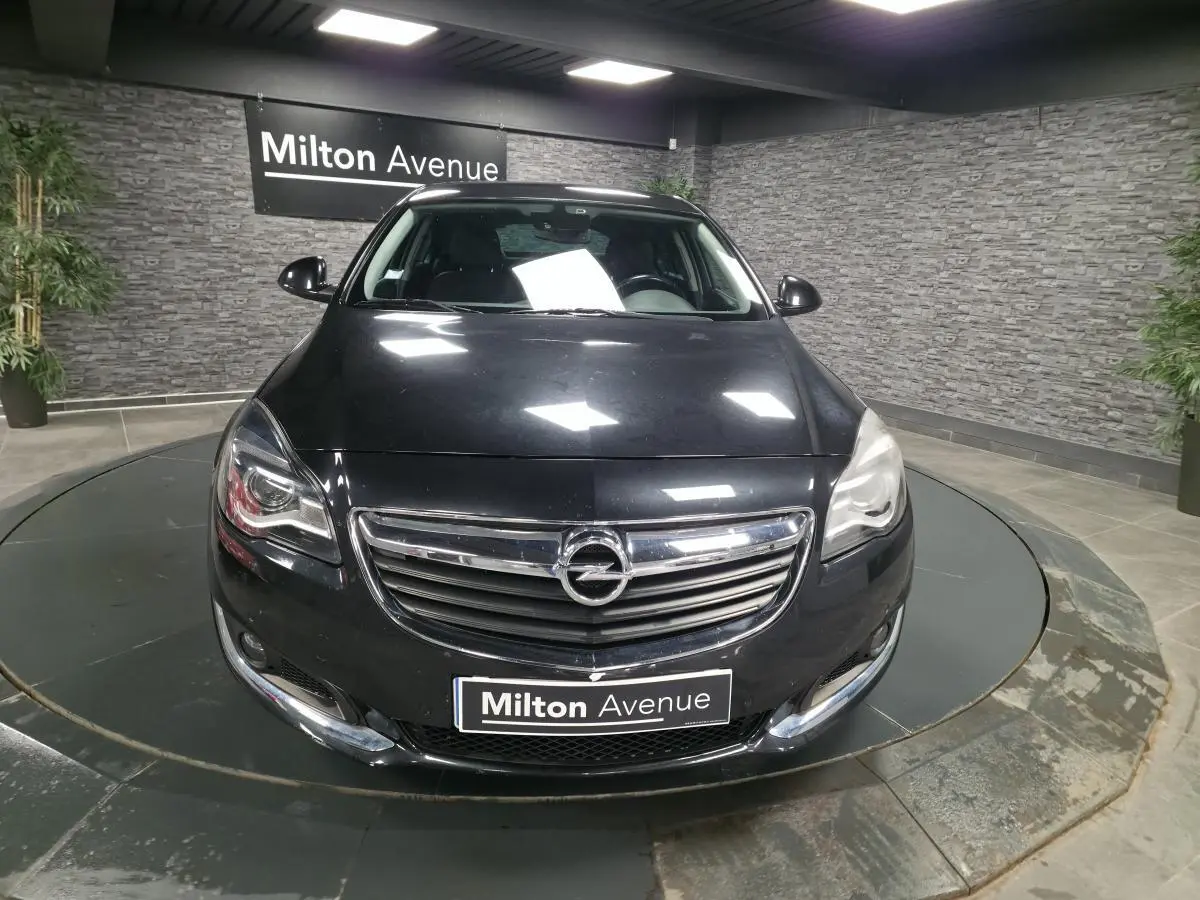 Vue frontale d'une Opel Insignia noire métallisée avec calandre chromée et phares allumés en showroom.