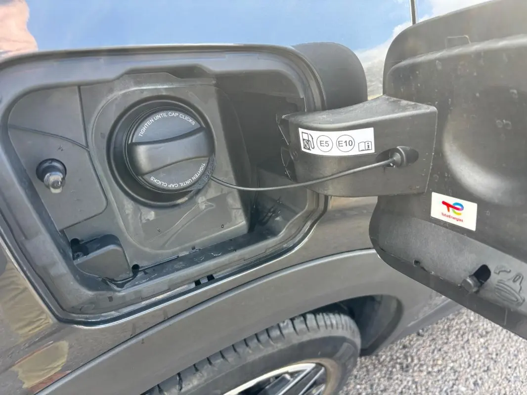 Vue rapprochée de la trappe à carburant côté gauche du Peugeot 3008 gris 2025 avec bouchon essence et jante alliage visible.