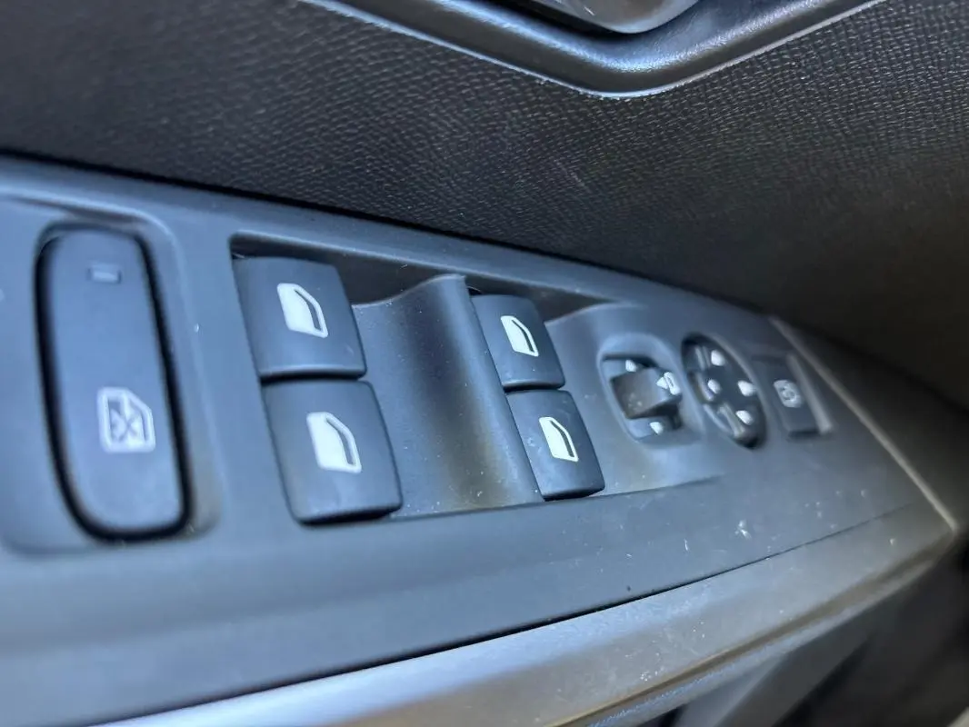 Gros plan sur les commandes des vitres et rétroviseurs côté gauche du Peugeot 3008 Hybrid gris, version 2025.