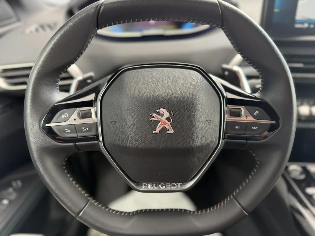 Volant cuir noir Mistral au design compact avec logo Peugeot, vue rapprochée centrée sur les commandes intégrées.